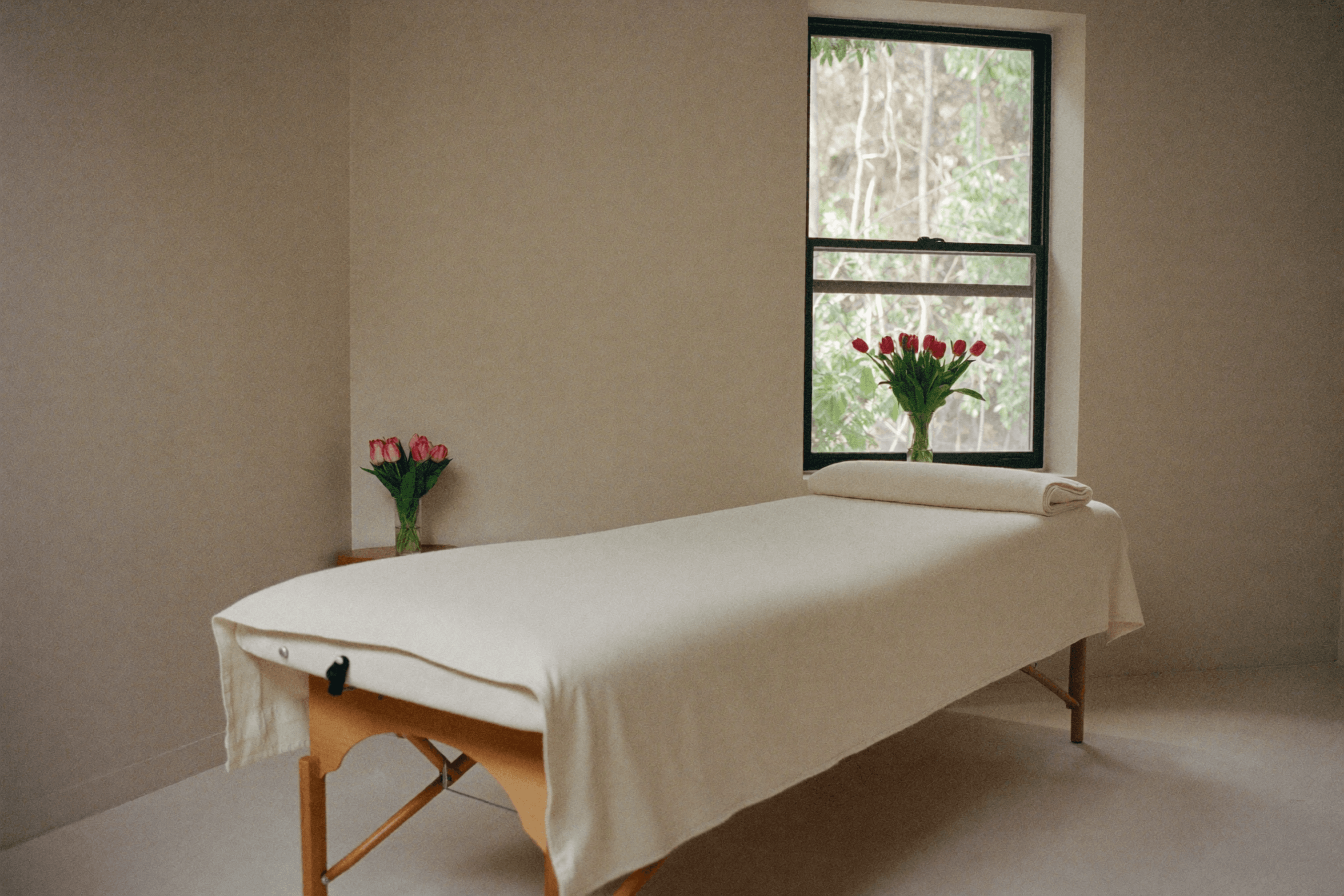 Calm, minimal treatment room with a linen-dressed table and fresh tulips